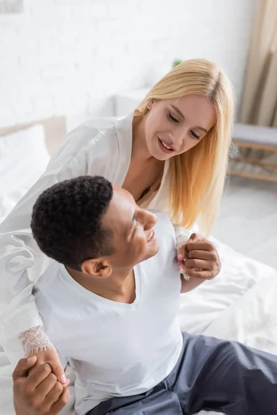 High angle view of blonde woman holding hands with african american boyfriend in bedroom — Stock Photo