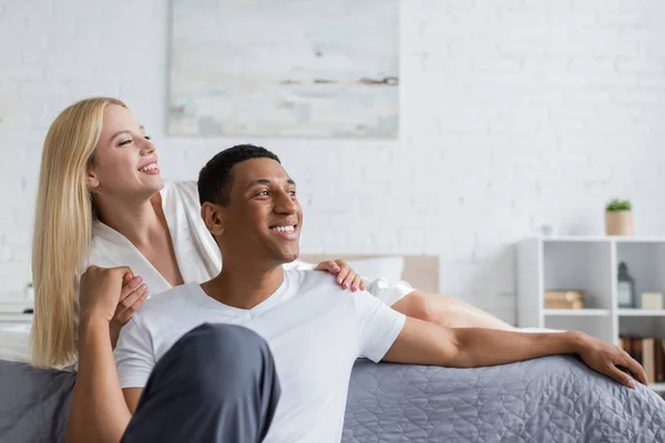 Positive african american man looking away while holding hands with young girlfriend in bedroom — Stock Photo