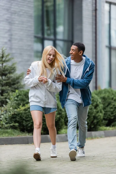 Pleine longueur de l'homme afro-américain étreignant petite amie blonde tout en marchant dans la ville — Photo de stock