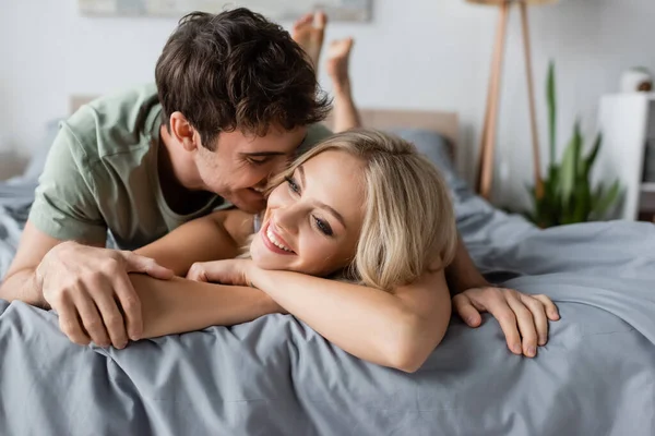 Cheerful man kissing blonde girlfriend on bed in morning — Stock Photo