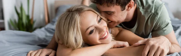Smiling young man kissing blonde girlfriend on bed in morning, banner — Stock Photo