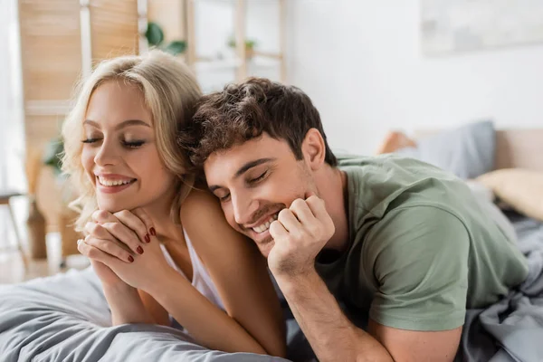 Jeune couple en pyjama couché les yeux fermés sur le lit le matin — Photo de stock