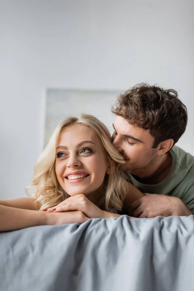 Man in pajama kissing pretty blonde girlfriend on bed — Stock Photo