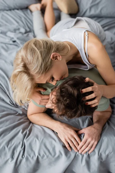 Vue aérienne de la femme blonde embrassant son petit ami en pyjama sur le lit — Photo de stock