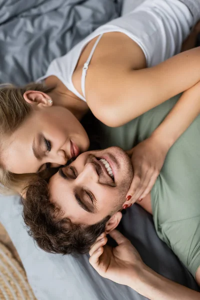Вид сверху молодой женщины в пижаме, трогающей шею положительного бойфренда на кровати — стоковое фото