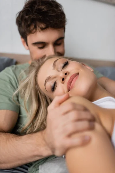 Blurred man hugging joyful blonde girlfriend on bed in morning — Stock Photo