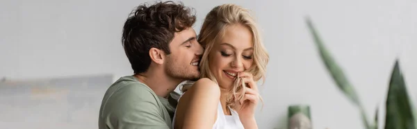 Hombre positivo en pijama besando a una joven novia en casa por la mañana, pancarta — Stock Photo