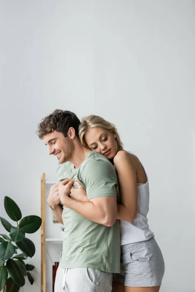 Mujer bonita en pijama abrazando novio en casa por la mañana - foto de stock