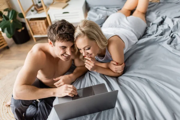 Vista de ángulo alto de alegre pareja sexy viendo la película en el ordenador portátil en la cama - foto de stock