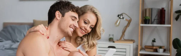 Young woman hugging muscular boyfriend with smartphone in bedroom, banner — Stock Photo
