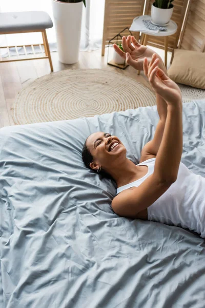 Fröhliche junge afrikanisch-amerikanische Frau gestikuliert, während sie zu Hause auf dem Bett liegt — Stockfoto