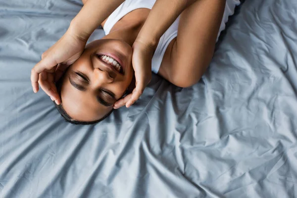 Top view of cheerful african american woman lying on bed at home — Stock Photo