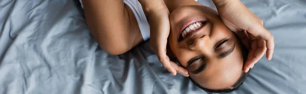 Вид зверху весела афроамериканка лежить на ліжку вдома, банер — стокове фото