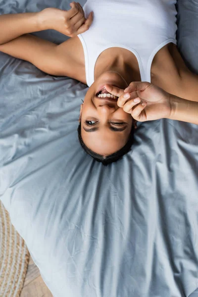 Vista superior da mulher americana africana alegre piscando enquanto deitado na cama em casa — Fotografia de Stock