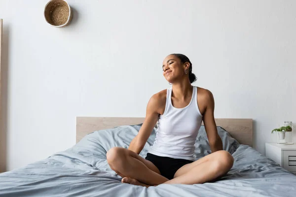 Jeune et heureuse femme afro-américaine en débardeur assis sur le lit — Photo de stock