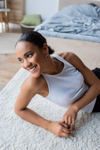 Young and joyful african american woman in tank top sitting on carpet — Stock Photo