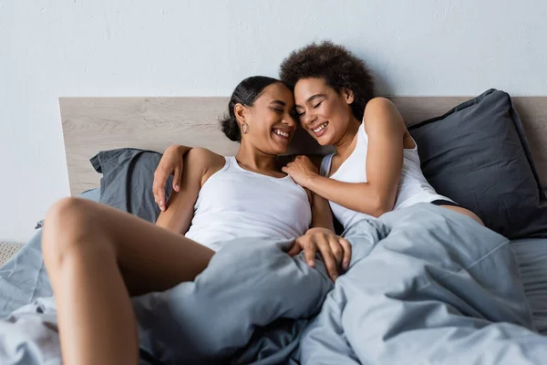 Happy and lesbian african american couple with closed eyes lying on bed at home — Stock Photo