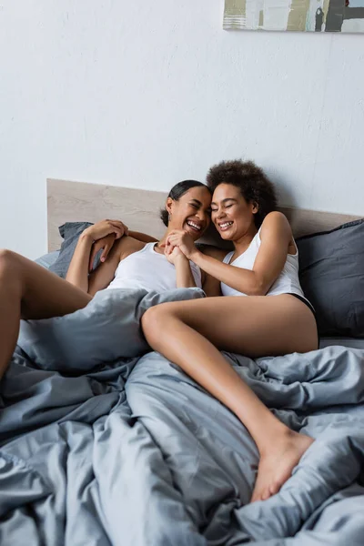Joyful and lesbian african american couple with closed eyes lying on bed at home — Stock Photo
