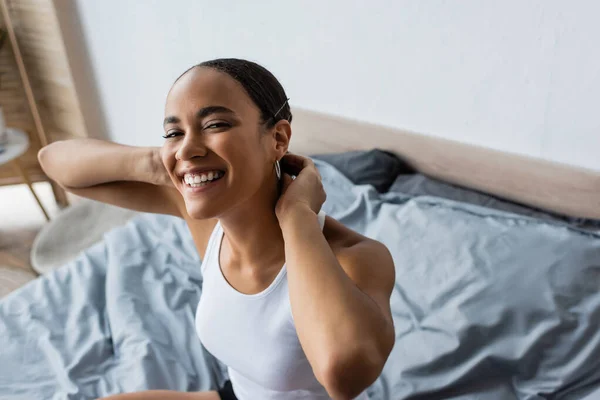 Vista ad alto angolo della donna afro-americana positiva sorridente e guardando la fotocamera in camera da letto — Foto stock