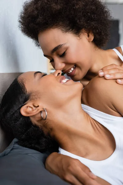 Joyeuse et lesbienne africaine américaine femme avec les yeux fermés embrasser petite amie sur le lit — Photo de stock