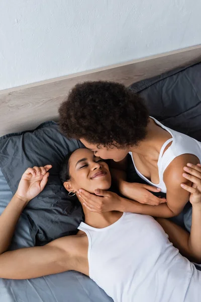 Top view of curly lesbian african american woman hugging happy girlfriend on bed — Stock Photo