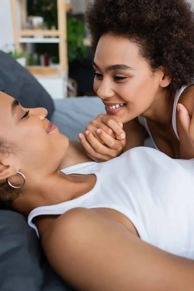 Alegre lésbicas africanas casal americano de mãos dadas enquanto deitado na cama — Fotografia de Stock