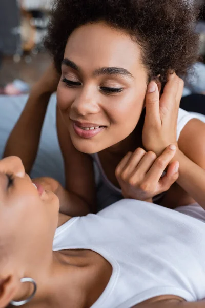 Cheerful lesbian african american couple hugging each other while lying on bed — Stock Photo