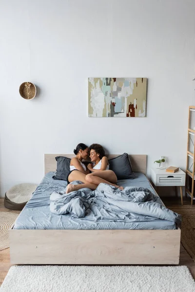 Усміхнена лесбіянка афро-американська пара обіймає один одного, лежачи в сучасній спальні — стокове фото