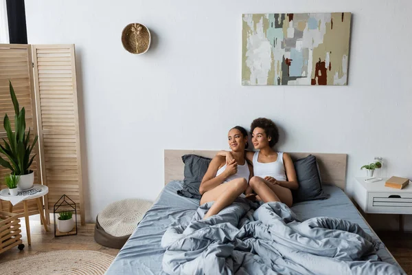 Fröhliche lesbische Afroamerikanerin umarmt Freundin im modernen Schlafzimmer — Stockfoto