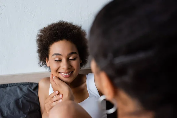 Lesbian african american woman touching cheek of happy girlfriend in bedroom — Stock Photo