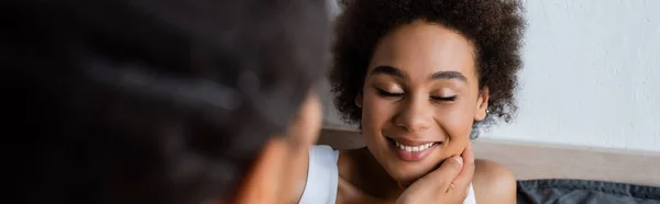 Lesbian african american woman touching cheek of happy girlfriend in bedroom, banner — Stock Photo