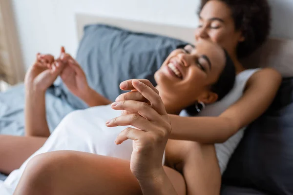Borrosa lesbiana africana americana pareja cogida de la mano mientras descansa en la cama - foto de stock
