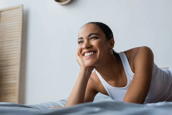 Retrato de la mujer afroamericana feliz sonriendo y mirando hacia otro lado en el dormitorio - foto de stock