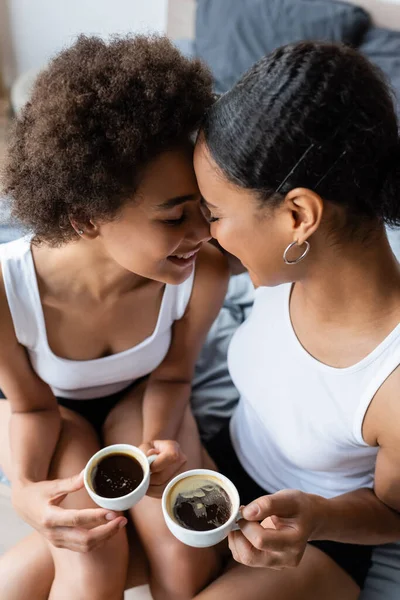 Vista superior de alegre pareja afroamericana lesbiana sosteniendo tazas de café - foto de stock