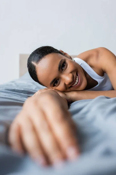 Pleased african american woman lying on bed and looking at camera — Stock Photo
