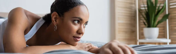 Young african american woman lying on bed and looking away, banner — Stock Photo
