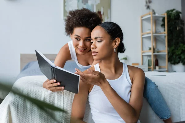 African american woman pointing with hand at notebook near girlfriend — Stock Photo
