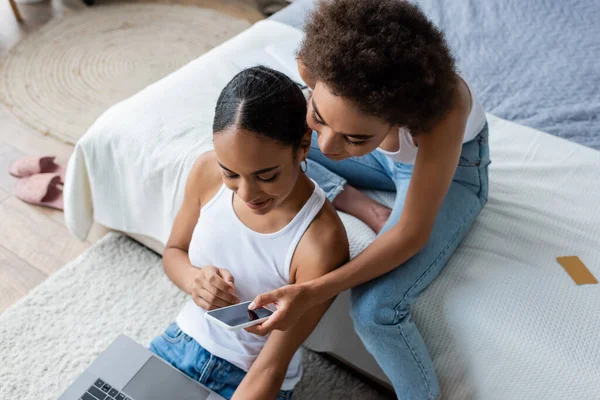Vue du haut de la jeune femme afro-américaine tenant smartphone près de petite amie avec ordinateur portable — Photo de stock