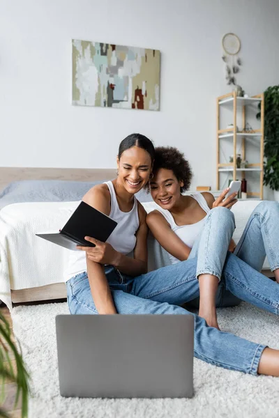 Mujeres afroamericanas felices y lesbianas mirando el ordenador portátil en el dormitorio - foto de stock