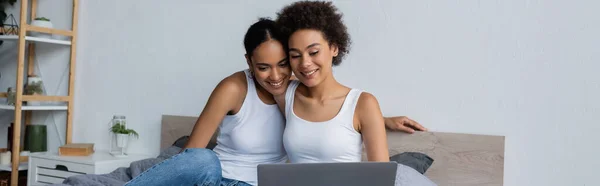 African american lesbian couple looking at laptop while watching movie in bedroom, banner — Stock Photo