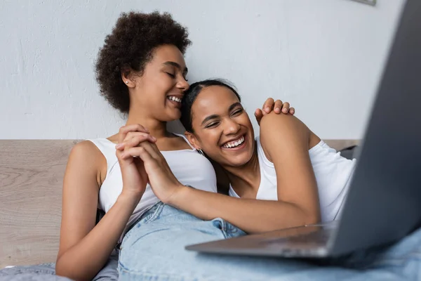 Alegre africano americano lesbiana pareja viendo película en laptop mientras cogido de la mano - foto de stock