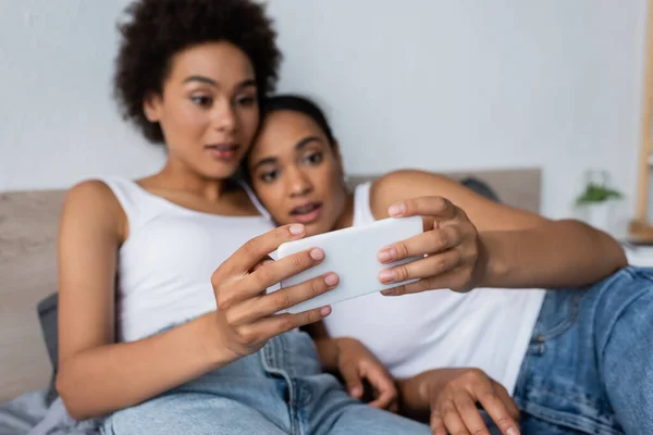Surpreso casal lésbico afro-americano usando smartphone no quarto — Fotografia de Stock