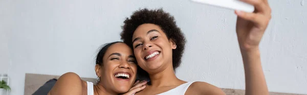 Щаслива афро-американська лесбіянка пара бере селфі на смартфон вдома, банер — стокове фото