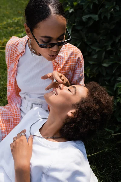 African american lesbian woman in sunglasses touching nose of happy girlfriend in green park — Stock Photo