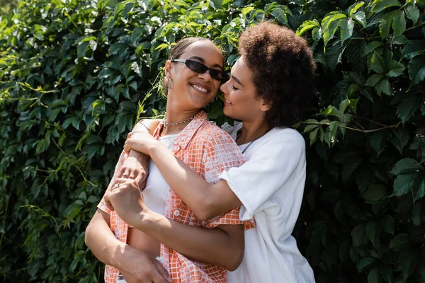 Glücklich afrikanisch-amerikanische lesbische Frau umarmt lächelnde Freundin mit Sonnenbrille — Stockfoto