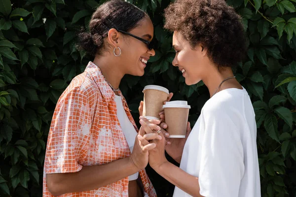 Freudige afrikanisch-amerikanische lesbische Frau mit Sonnenbrille hält Händchen mit lächelnder Freundin — Stockfoto