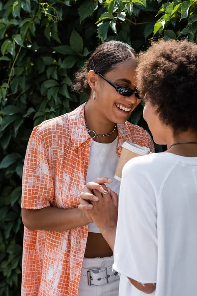 Happy african american lesbian woman in sunglasses holding hands with girlfriend — Stock Photo