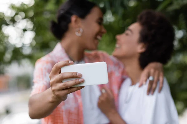 Positivo africano americano lesbiana pareja tomando selfie en borrosa fondo - foto de stock