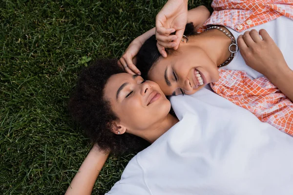 Vue de dessus des femmes lesbiennes africaines américaines heureuses allongées sur l'herbe — Photo de stock