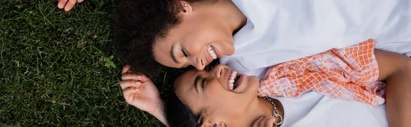 Вид сверху на счастливых африканских лесбиянок, лежащих на траве, баннер — стоковое фото